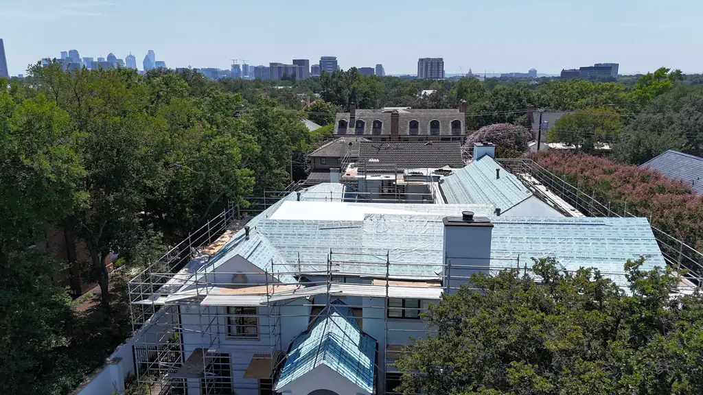 Tile roof replacement in progress, with scaffolding around the house and the Dallas skyline behind