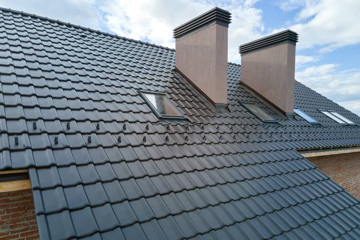 closeup of attic windows and brick chimneys on a house roof covered with ceramic shingles